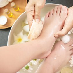 foot washing in spa before treatment. spa treatment and product for female feet and hand spa. white flowers in ceramic bowl with water for aroma therapy at spa.