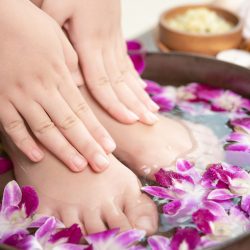 closeup view of woman soaking her hand and feet in dish with water and flowers on wooden floor. Spa treatment and product for female feet and hand spa. orchid flowers in ceramic bowl.